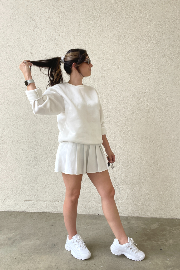 White outfit inspo for the summer featuring a white tennis skirt, white sweatshirt, and white chunky sneakers