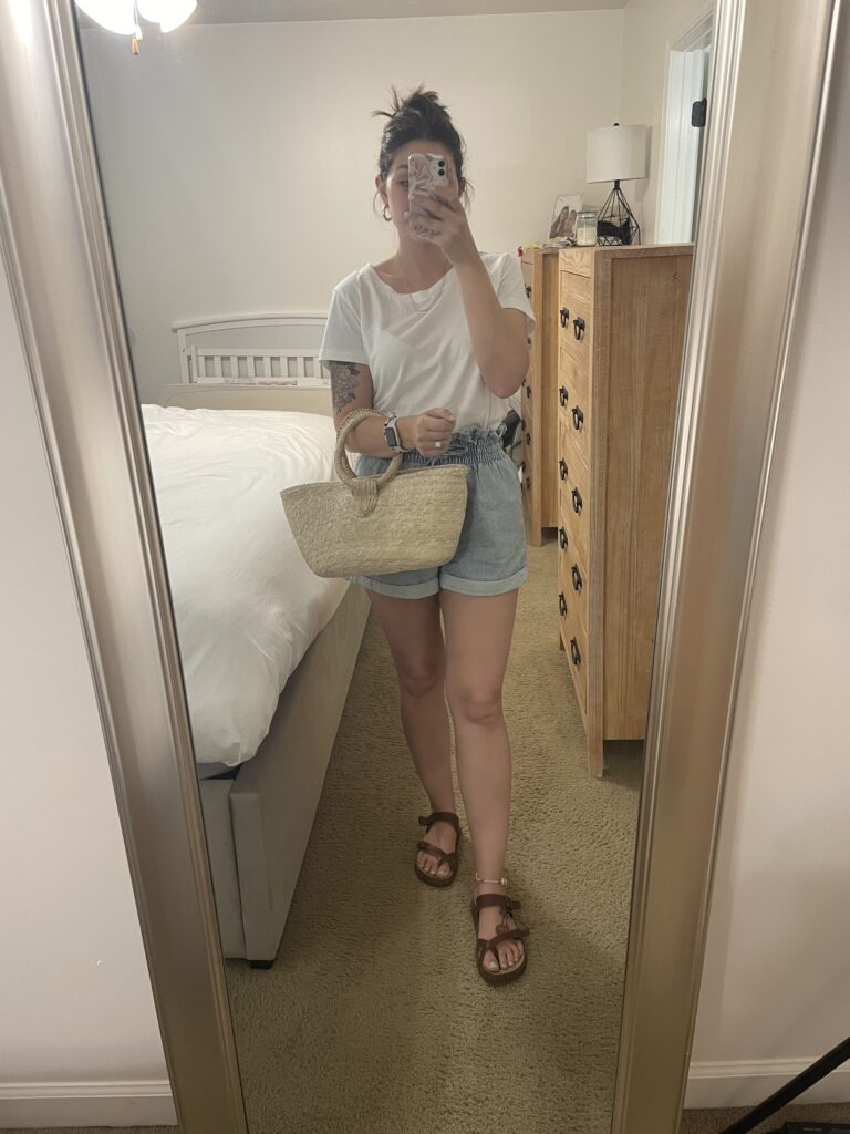 mirror outfit picture of a white teeshirt, blue jean paperbag shorts, straw purse, and dark brown sandals